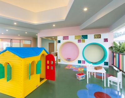 Bright, playful children's playroom with yellow playhouse, small white table and chairs, colorful wall cutouts, and a cheerful, inviting atmosphere.