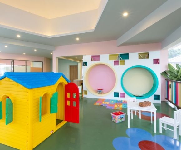 Bright, playful children's playroom with yellow playhouse, small white table and chairs, colorful wall cutouts, and a cheerful, inviting atmosphere.