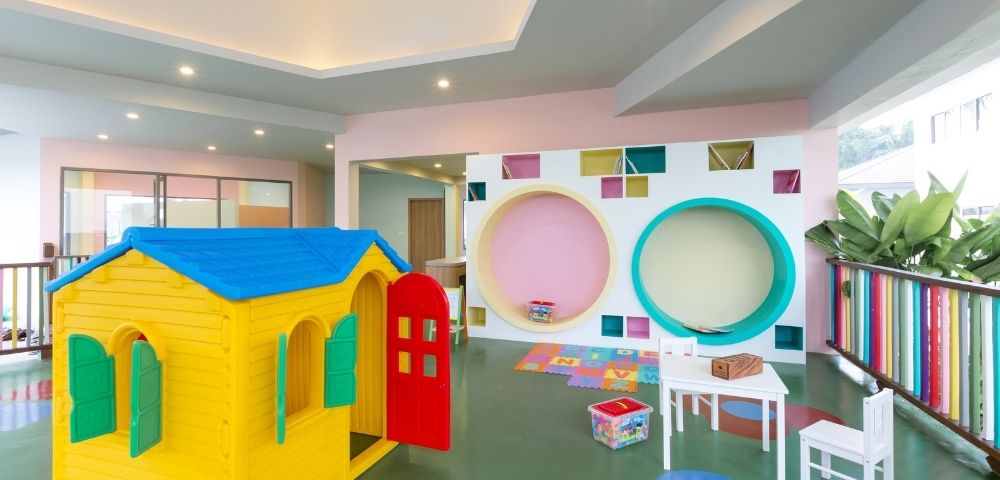 Bright, playful children's playroom with yellow playhouse, small white table and chairs, colorful wall cutouts, and a cheerful, inviting atmosphere.