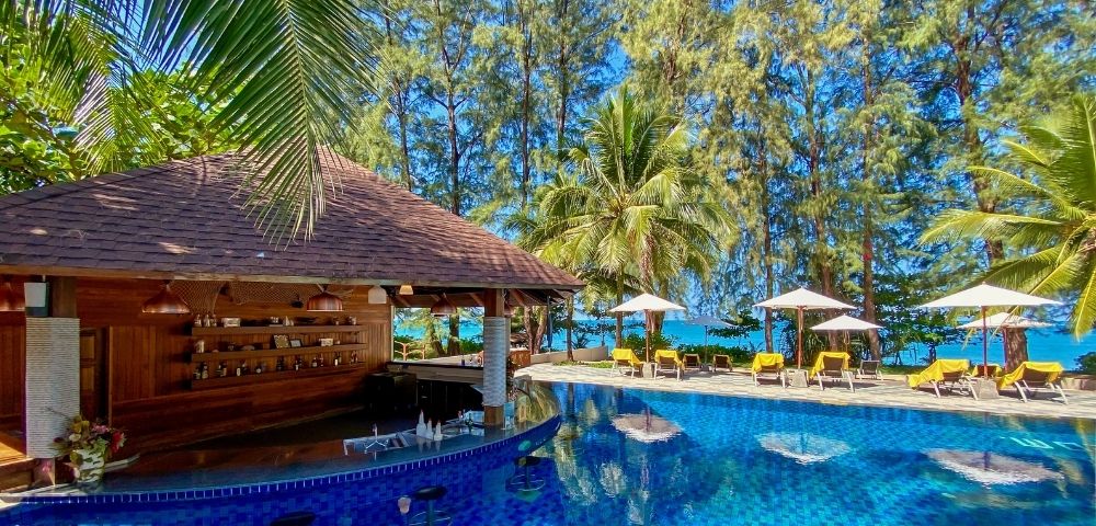 Tropical pool scene with a swim-up bar, surrounded by sun loungers and umbrellas. Palm trees and a serene ocean view create a relaxed, sunny atmosphere.