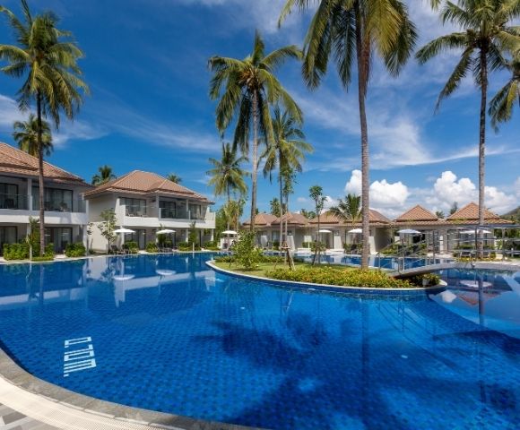 Luxurious resort pool under a vibrant blue sky, surrounded by tall palm trees and elegant villas. The scene conveys a relaxing and serene tropical ambiance.