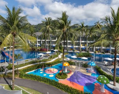 Tropical resort with two pools surrounded by palm trees. Colorful water play area for children with slides and mushroom fountains. Relaxing atmosphere.