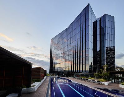 Modern glass building reflecting the sunset sky stands beside a sleek rooftop pool with lounge chairs, creating a serene and luxurious atmosphere.