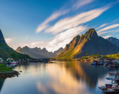 Picturesque rural scene with red houses, lush greenery, and mountains reflected in a serene fjord