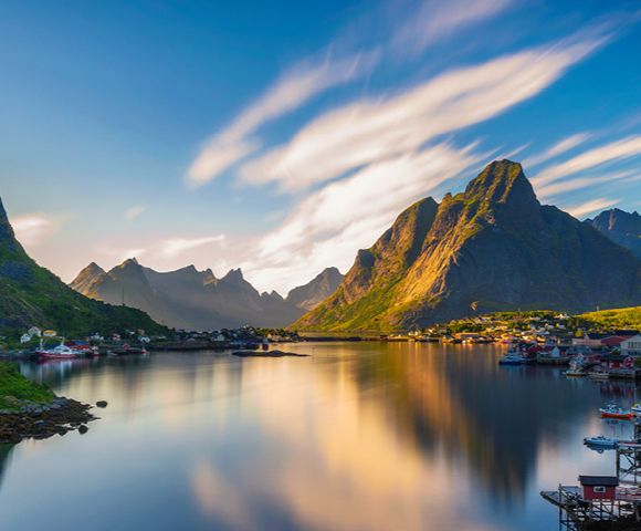 Picturesque rural scene with red houses, lush greenery, and mountains reflected in a serene fjord