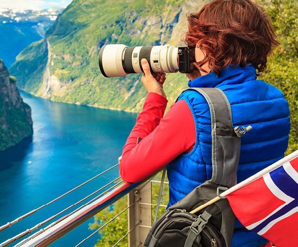Stunning fjord landscape with steep green cliffs, deep blue water, and a Norwegian flag in the foreground