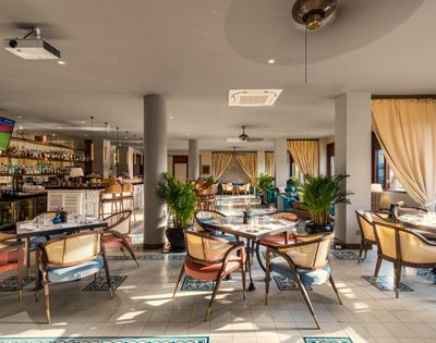 Modern restaurant interior with wooden furniture, potted plants, and soft lighting. Open layout with a warm, inviting atmosphere.