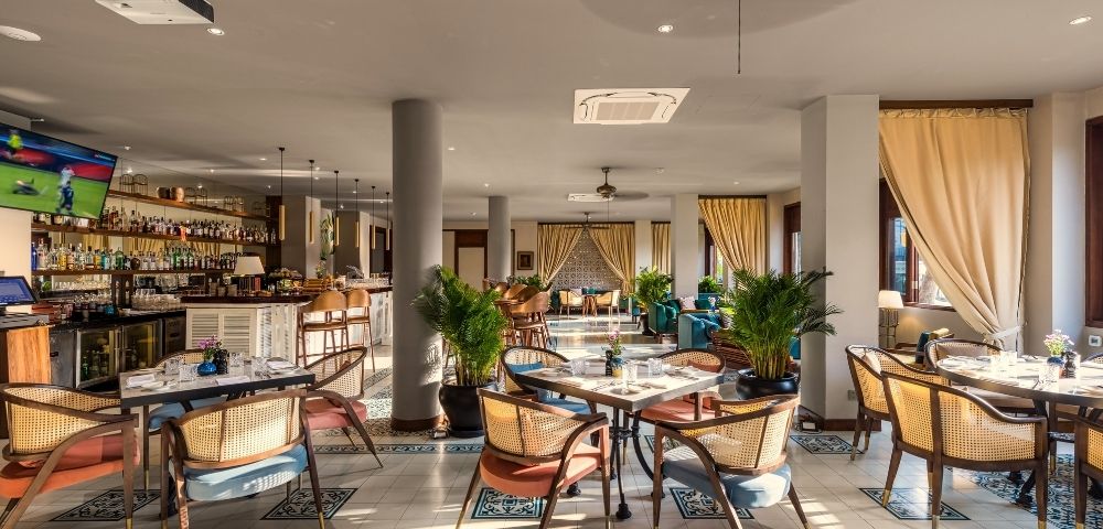 Modern restaurant interior with wooden furniture, potted plants, and soft lighting. Open layout with a warm, inviting atmosphere.