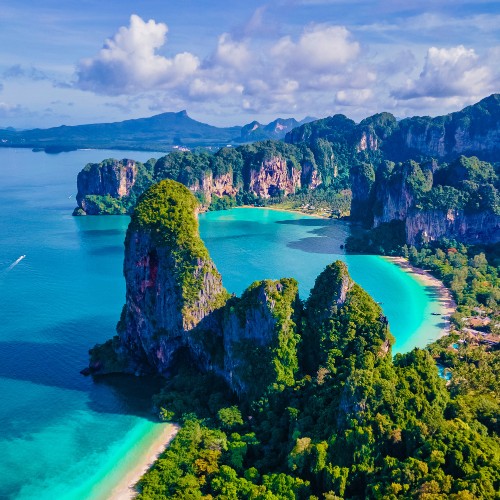Aerial view of a tropical coastline with turquoise waters, lush greenery, and steep cliffs under a sunny blue sky. The tranquil scene evokes a sense of serenity.