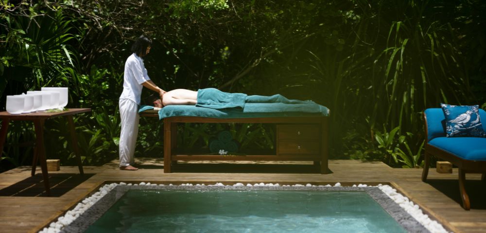 A woman relaxes while receiving a massage in a tranquil pool setting.