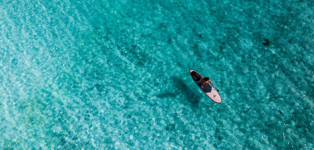 Aerial view of a person riding a paddleboard on the ocean waves, showcasing the vast blue water below.