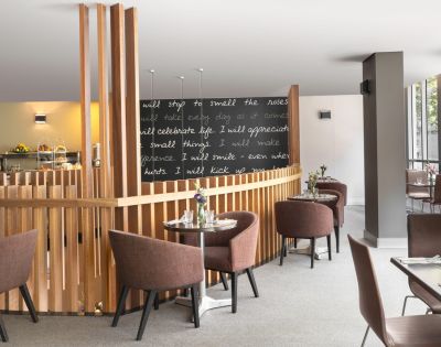 Modern cafe interior with brown chairs and round tables on a light carpet. A blackboard displays inspirational quotes in white script, adding a cozy vibe.