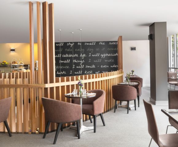 Modern cafe interior with brown chairs and round tables on a light carpet. A blackboard displays inspirational quotes in white script, adding a cozy vibe.