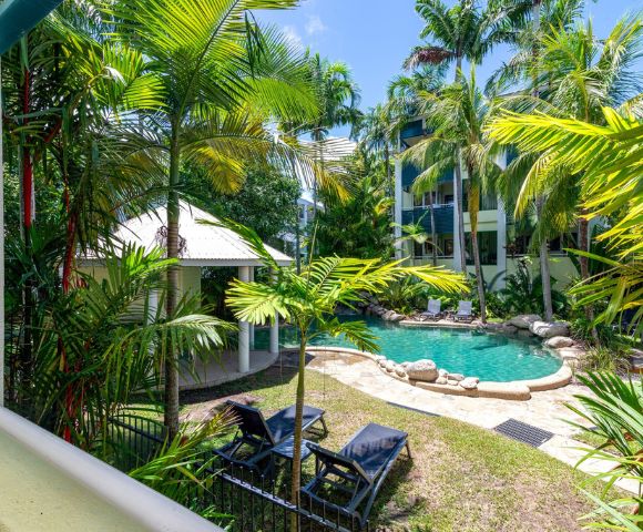 Tropical oasis with lush palm trees surrounding a curved pool. Two lounge chairs face the serene water, creating a tranquil, resort-like atmosphere.