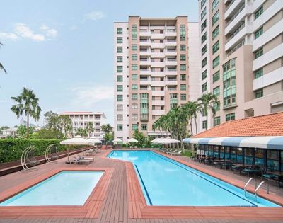 A modern outdoor swimming pool area with a smaller pool, surrounded by high-rise buildings and palm trees. Lounge chairs and umbrellas offer a relaxing vibe.