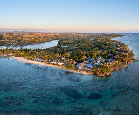 Aerial view of a tropical island with lush greenery and a sandy beach surrounded by clear blue water, conveying a serene and idyllic atmosphere.