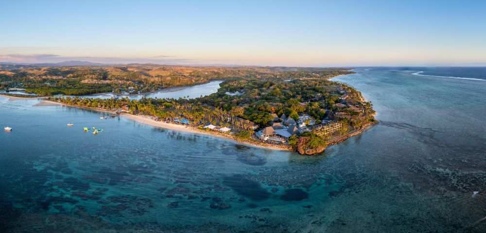 Aerial view of a tropical island with lush greenery and a sandy beach surrounded by clear blue water, conveying a serene and idyllic atmosphere.