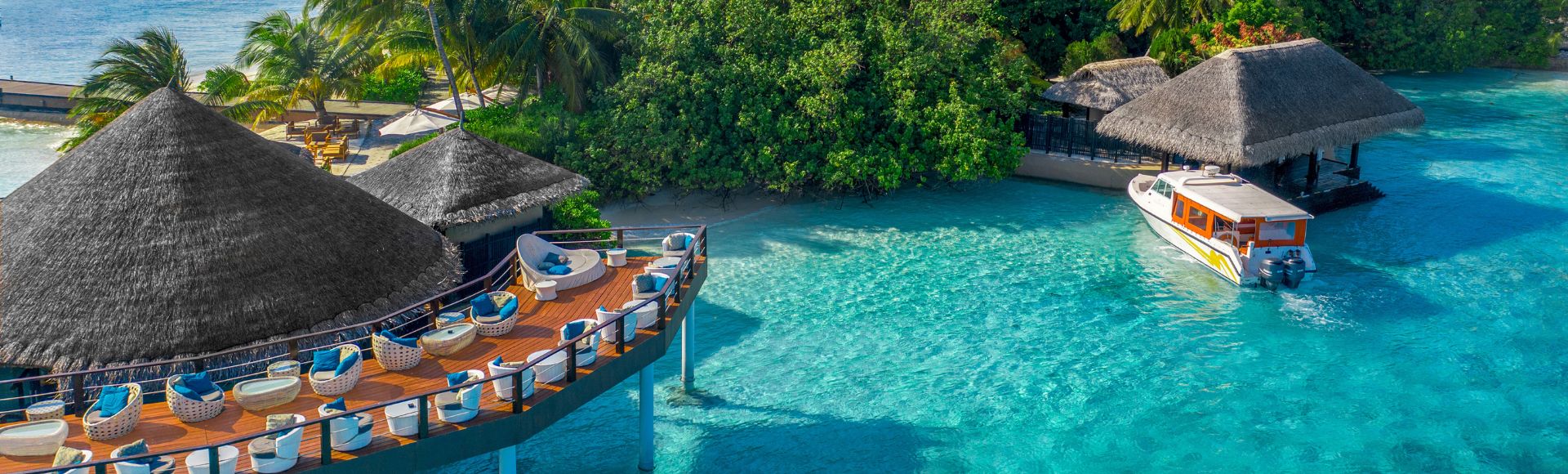 Overwater bungalows surrounded by turquoise waters, with a boat near a tropical island and lush greenery under a sunny sky.