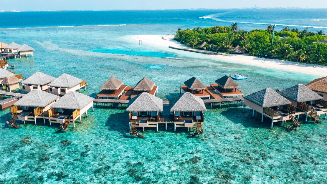 Overwater bungalows on clear turquoise waters, surrounded by lush greenery and a sandy beach in a tropical paradise.