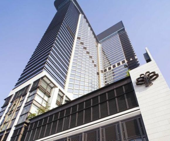 A modern skyscraper with sleek glass panels and geometric patterns rises into a clear blue sky, conveying a sense of grandeur and sophistication.