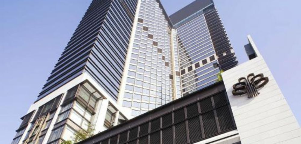 A modern skyscraper with sleek glass panels and geometric patterns rises into a clear blue sky, conveying a sense of grandeur and sophistication.