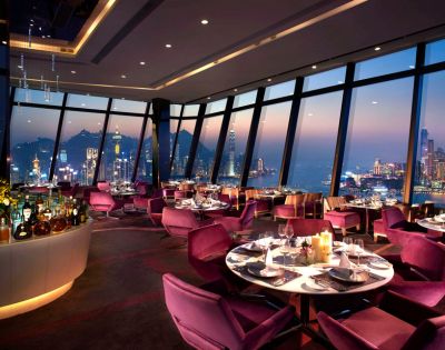 Luxurious restaurant interior with purple chairs and candlelit tables by large windows. Offers panoramic city skyline view at sunset, creating an elegant ambiance.