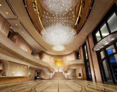Elegant hotel lobby with grand staircase, featuring a large, ornate chandelier. Soft lighting and marble floors create a luxurious and welcoming atmosphere.