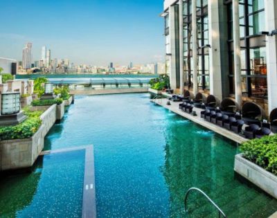 Luxurious rooftop pool overlooking a city skyline. Modern architecture, lounge chairs, greenery, and a serene, sunny atmosphere create a sense of relaxation.