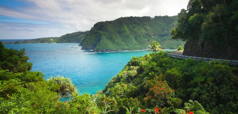Lush green cliffs overlook a vibrant turquoise sea, with winding roads cutting through the scenic landscape under a partly cloudy sky.