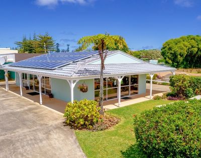A modern, sunlit house with solar panels on a white roof, surrounded by lush greenery and a clear blue sky, conveying eco-friendly tranquility.
