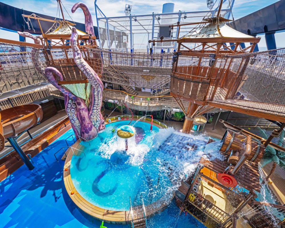 Colorful water playground with giant purple octopus tentacles, splashing water, and wooden structures. Exciting, playful atmosphere under a blue sky.