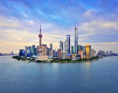 Shanghai skyline at dusk, showcasing iconic skyscrapers like the Oriental Pearl Tower. Calm river in foreground, under a sky painted with soft clouds.
