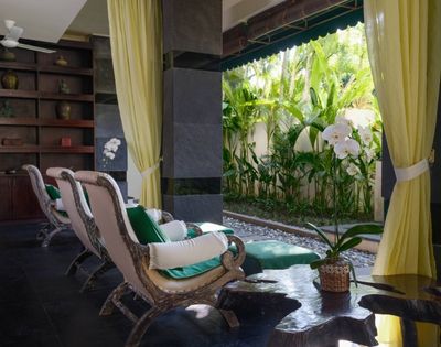 Spacious room with elegant chairs and green cushions facing lush garden. Open curtains reveal vibrant plants, creating a serene, tropical ambiance.