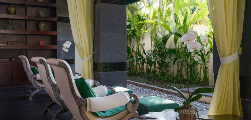 Spacious room with elegant chairs and green cushions facing lush garden. Open curtains reveal vibrant plants, creating a serene, tropical ambiance.