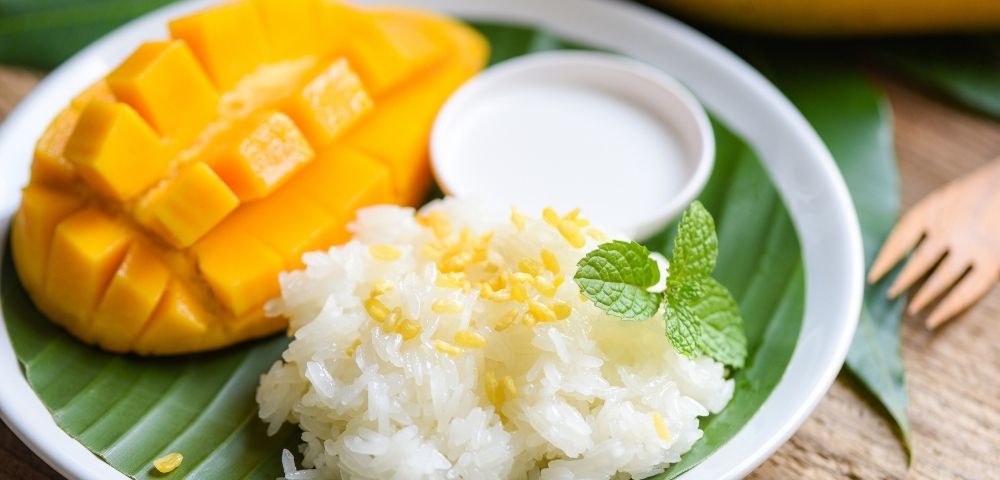 Mango slices and fluffy rice served together on a white plate, creating a colorful and appetizing dish.