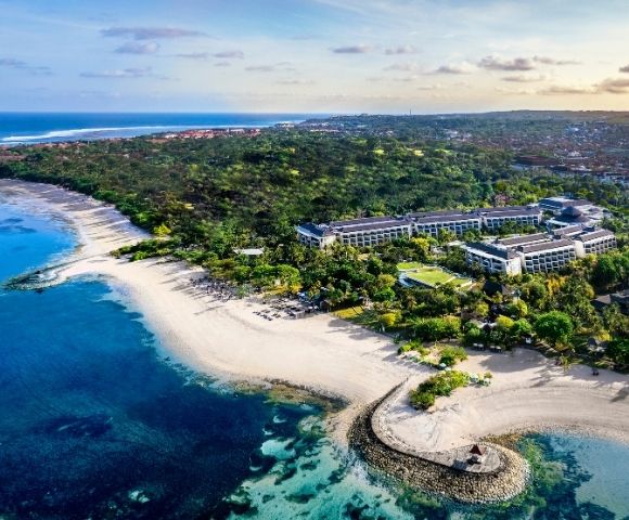 Aerial view of a coastal resort surrounded by lush greenery. Pristine beaches and turquoise waters evoke a serene, tropical paradise.