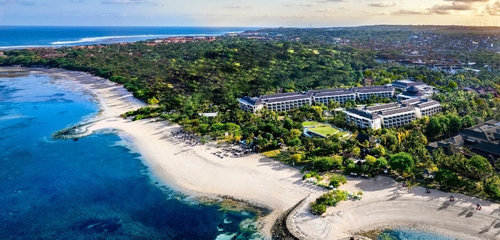 Aerial view of a coastal resort surrounded by lush greenery. Pristine beaches and turquoise waters evoke a serene, tropical paradise.