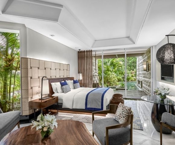 Luxurious hotel room with a plush bed, wooden furnishings, and modern decor. Glass doors open to a lush garden, creating a serene and inviting atmosphere.