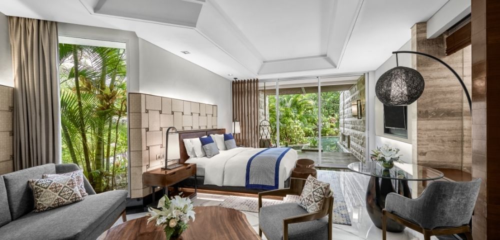 Luxurious hotel room with a plush bed, wooden furnishings, and modern decor. Glass doors open to a lush garden, creating a serene and inviting atmosphere.