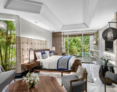 Luxurious hotel room with a plush bed, wooden furnishings, and large windows revealing a lush garden. Modern decor creates a tranquil, inviting ambiance.