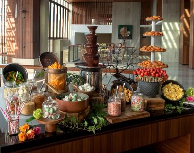 A chocolate fountain surrounded by assorted treats, including fruits, marshmallows, and pastries, creating a lavish, inviting dessert display.