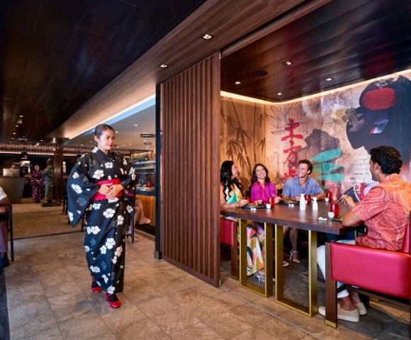 A restaurant scene featuring a woman in a traditional kimono walking by, while a group enjoys their meal at a table.