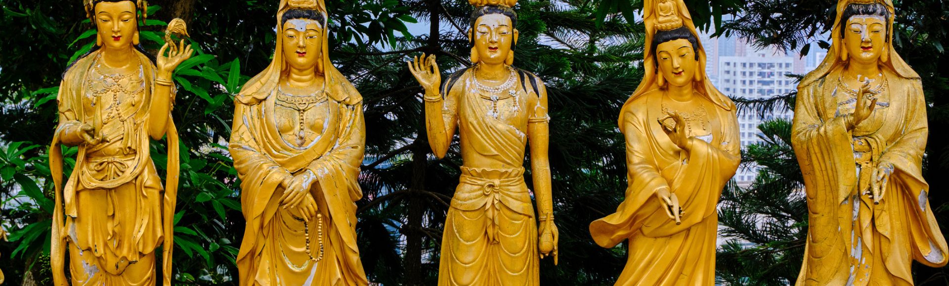 Three golden Buddhist statues stand in serene poses, surrounded by lush greenery. The central statue raises a hand, conveying tranquility and peace.