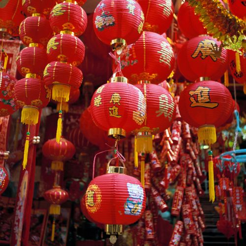 Vibrant display of red Chinese lanterns with gold calligraphy, symbolizing celebration and good fortune. The festive scene conveys warmth and joy.