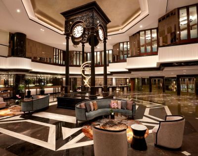 Elegant hotel lobby featuring a central ornate clock, modern furniture, and sleek lighting. The ambiance is luxurious and welcoming, with warm tones.