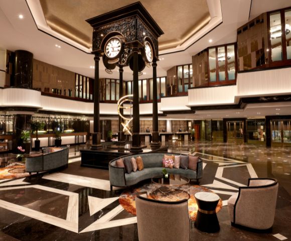 Elegant hotel lobby featuring a central ornate clock, modern furniture, and sleek lighting. The ambiance is luxurious and welcoming, with warm tones.