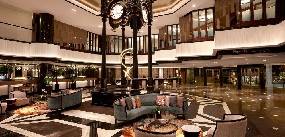 Elegant hotel lobby featuring a central ornate clock, modern furniture, and sleek lighting. The ambiance is luxurious and welcoming, with warm tones.