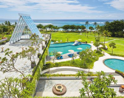 Luxurious beachfront resort with a glass chapel, lush gardens, and two turquoise pools overlooking the ocean. Sunny, tropical, and serene atmosphere.