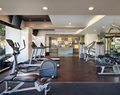 Modern gym interior with treadmills, exercise bikes, and weight machines on dark wooden floors. Bright lighting creates a clean, inviting atmosphere.