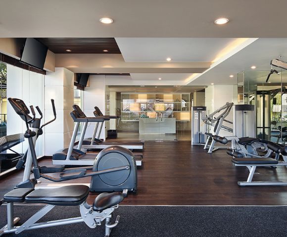 Modern gym interior with treadmills, exercise bikes, and weight machines on dark wooden floors. Bright lighting creates a clean, inviting atmosphere.